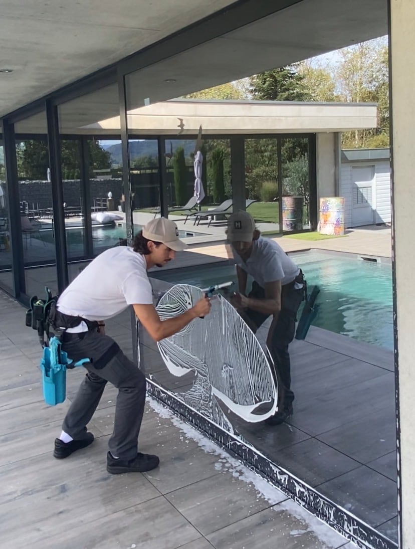 Deux techniciens Hyaluxe nettoyant une grande baie vitrée devant une piscine